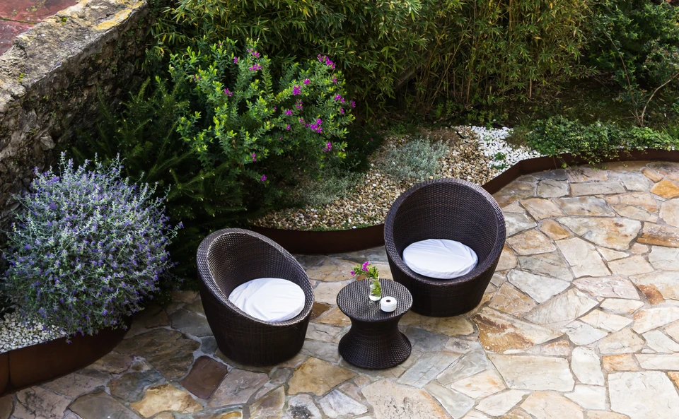 Terrasse extérieure en dalles de pierre naturelle avec salon de jardin en résine tressée anthracite comprenant deux fauteuils coques avec coussins blancs et table basse ronde